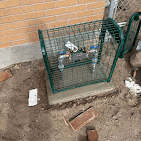 Backflow preventer installed inside a green protective cage on a concrete pad