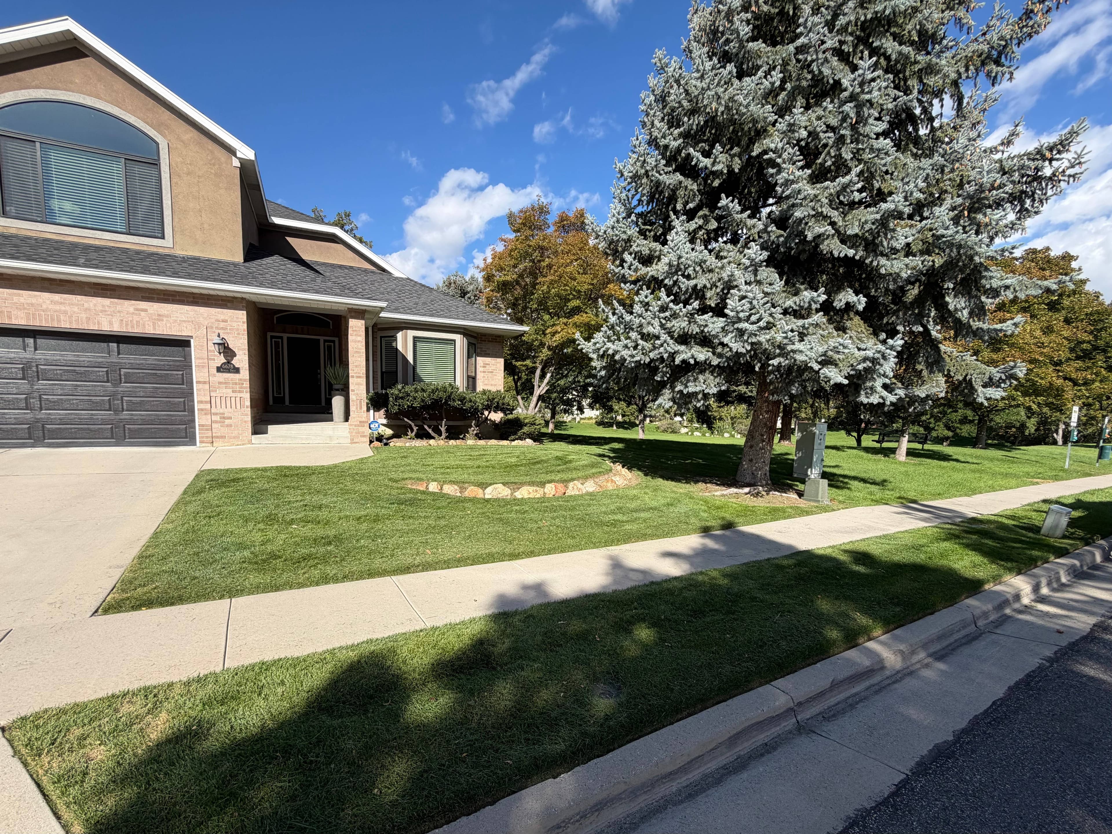 Healthy green lawn with a curved rock border in front of a brick and stucco home
