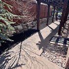 Concrete walkway under a pergola lined with fresh mulch and rock beds