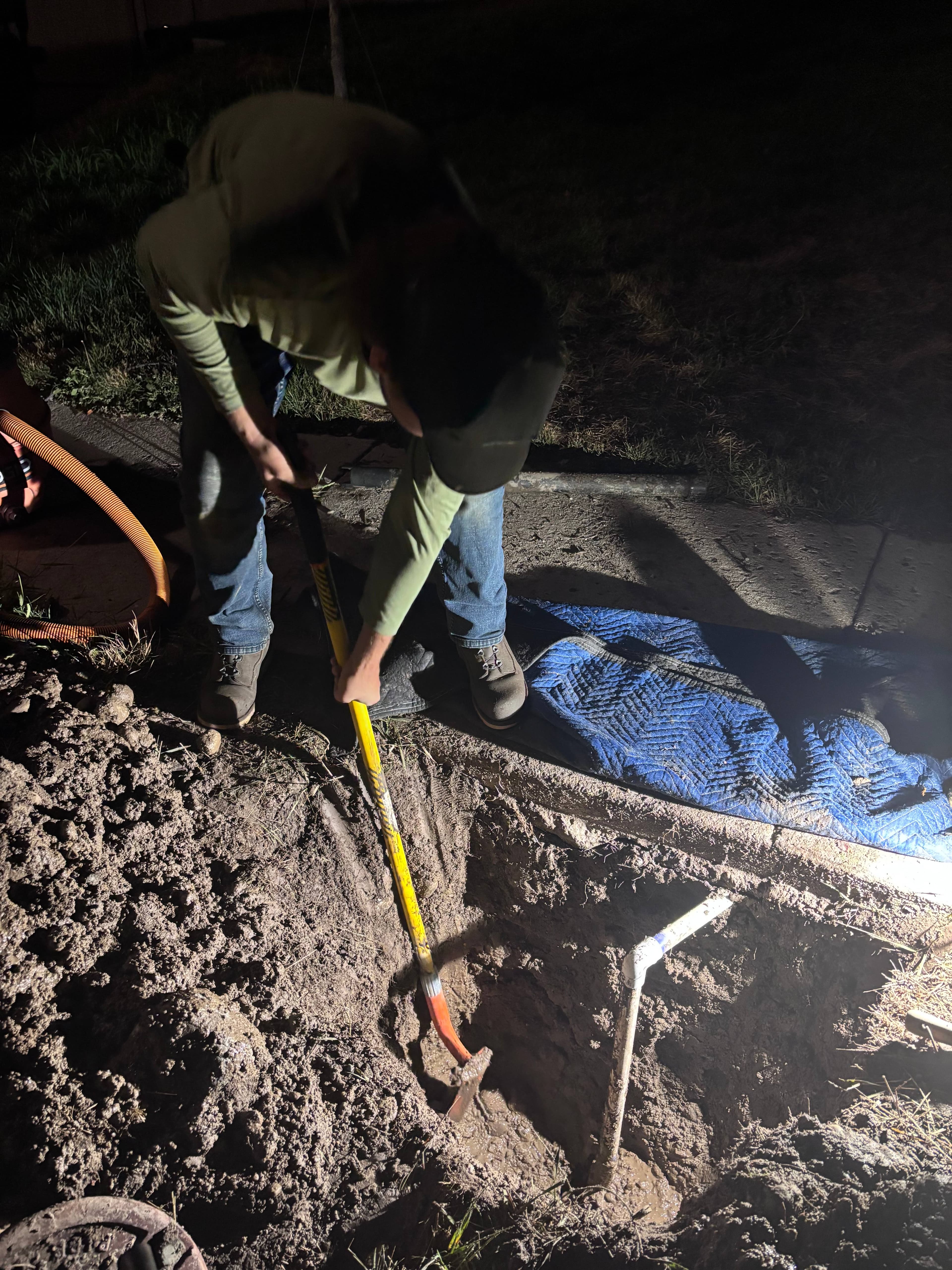 Technician excavating a muddy sprinkler valve area at night
